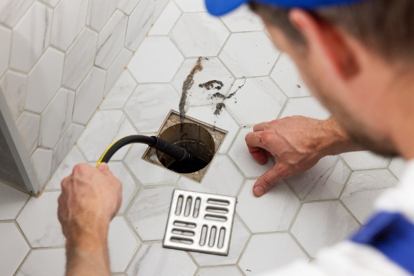 plumber cleaning clogged shower drain with snake