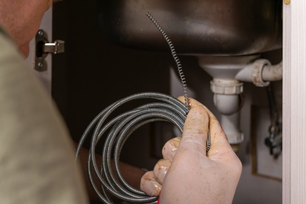 plumber holding drain snake under kitchen sink